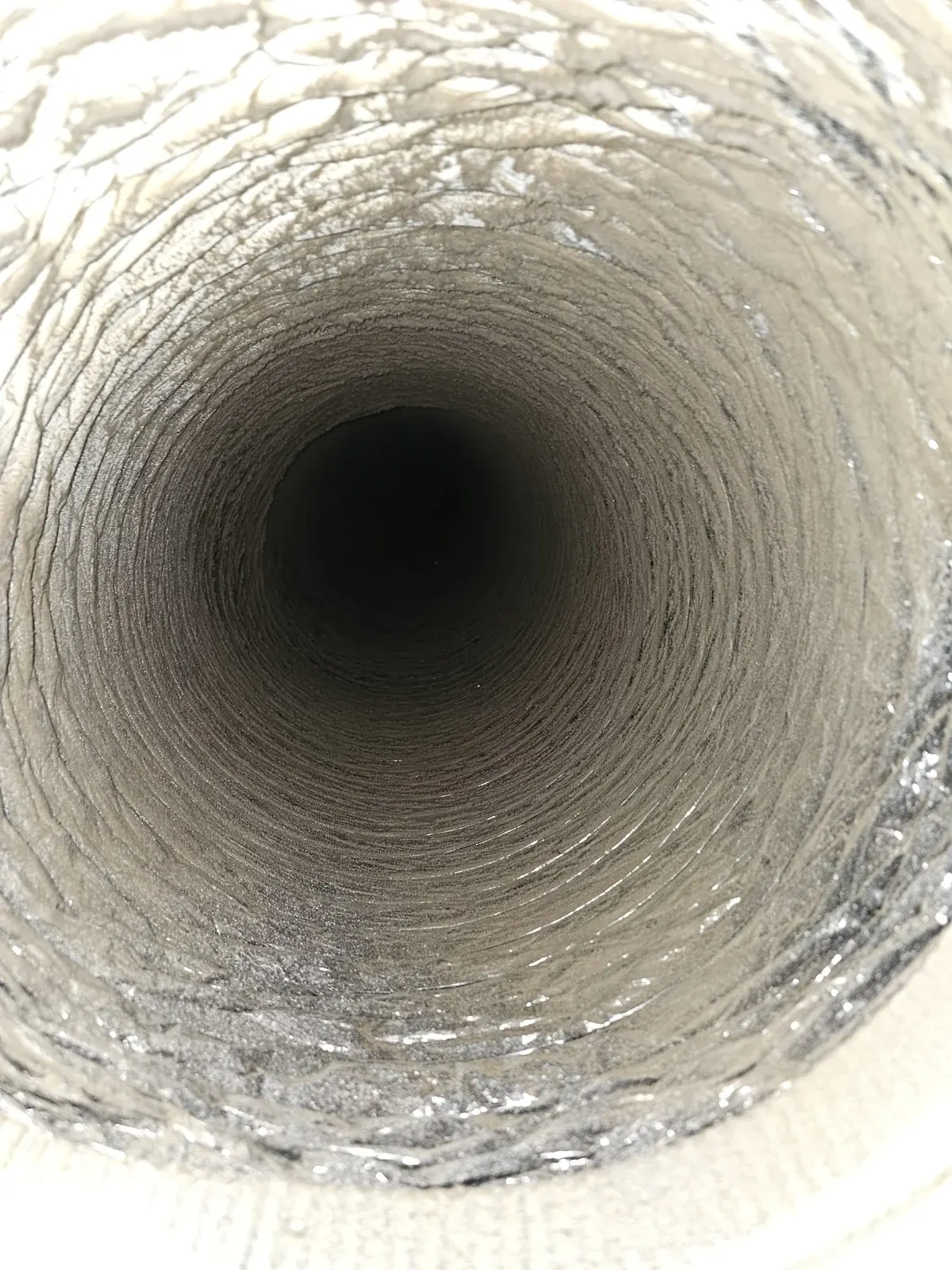 Before: round flexible duct with gray dust over the silver foil