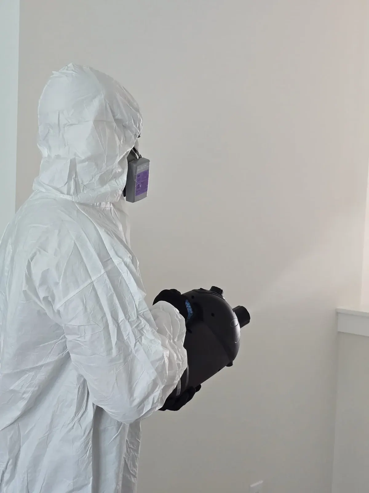 Technician in a protective suit and respirator running a fogger with visible mist