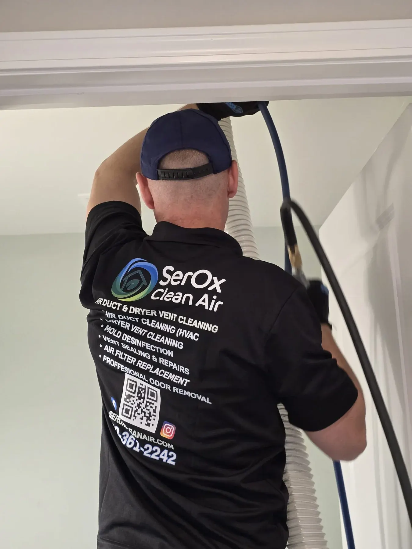 Back of a black SerOx polo listing the services while a ceiling vent is cleaned