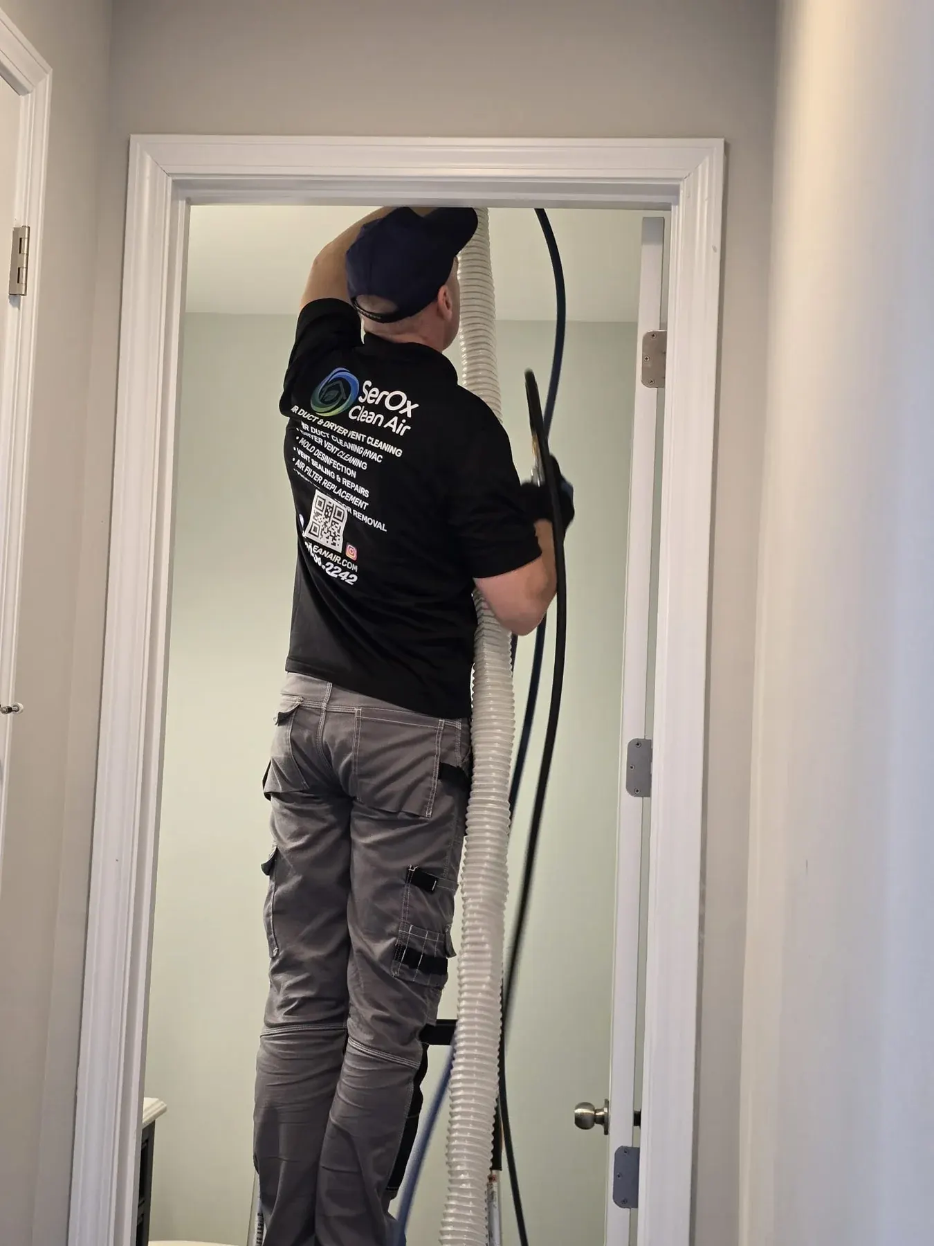 Serhii on a ladder in a doorway, working a hose into a ceiling vent