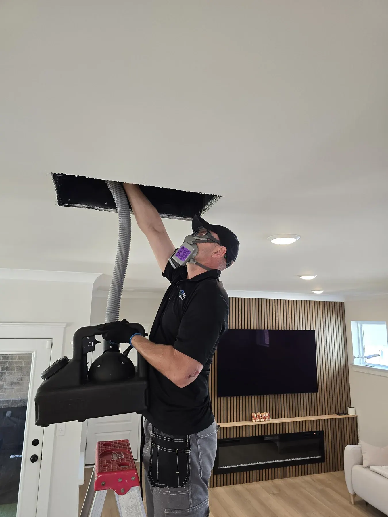 Technician in a respirator treating an open ceiling duct with a sprayer in a living room