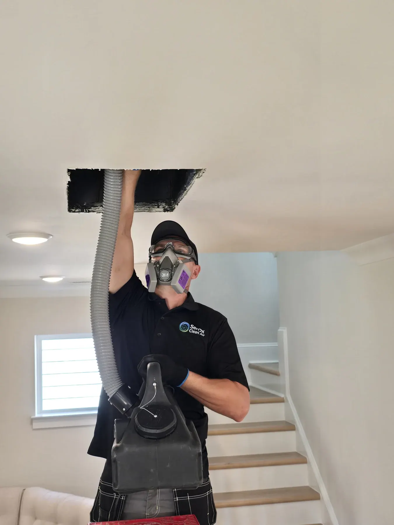 Technician holding a vacuum hose connected to an open ceiling duct near the stairs