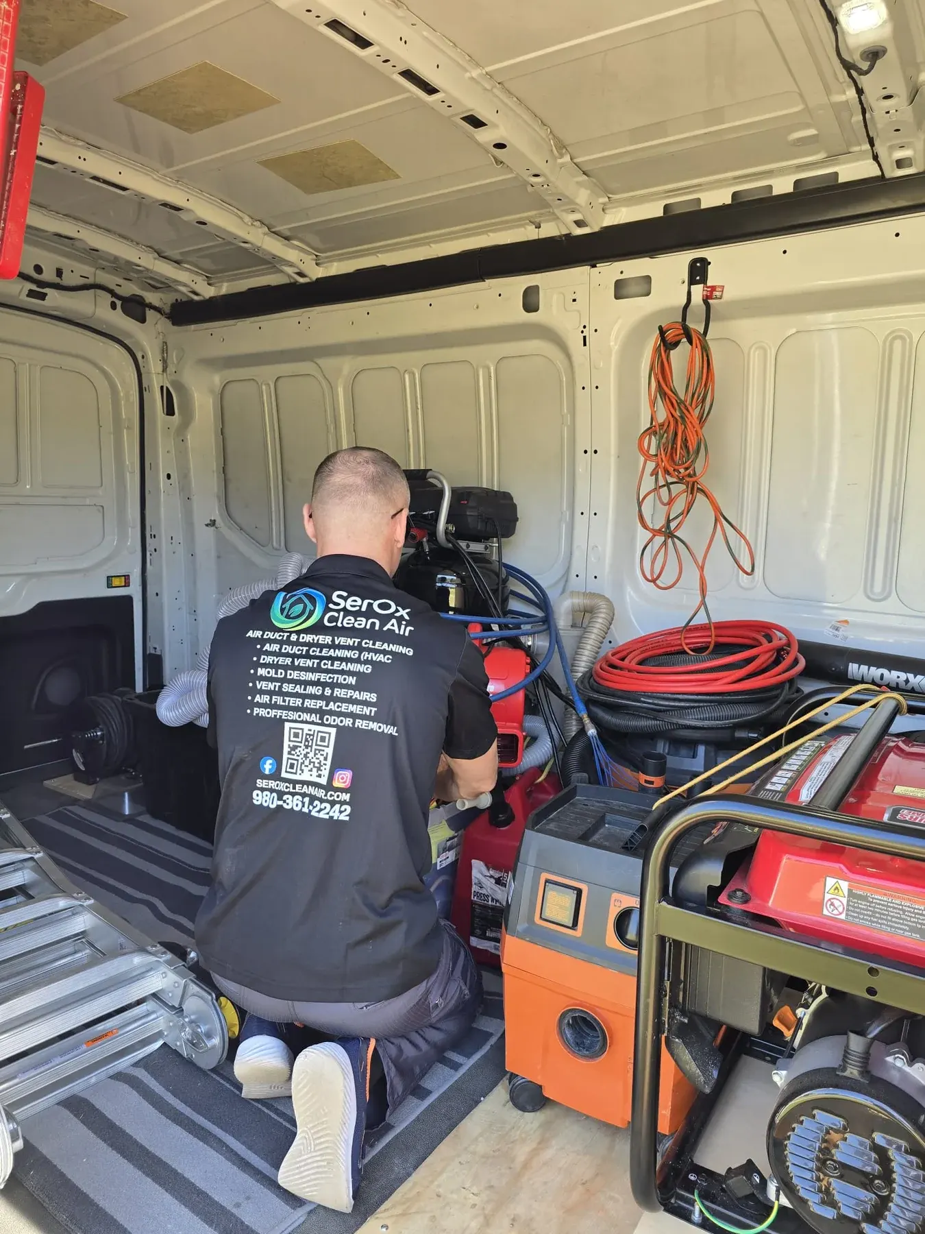 Serhii kneeling in the SerOx van next to the generator, compressor and hose reels